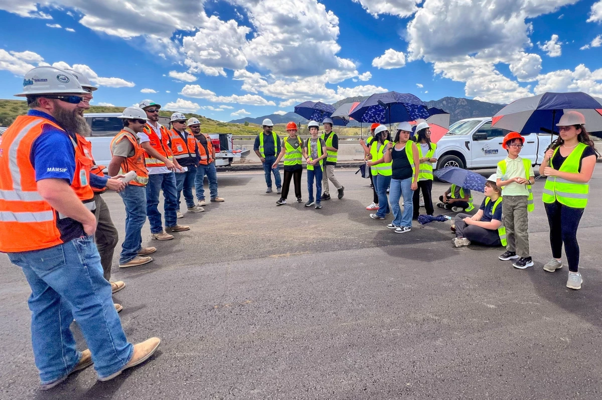 SEMA staff introduce the NIST students to the project site. Students are using umbrellas to protect them from the sun.