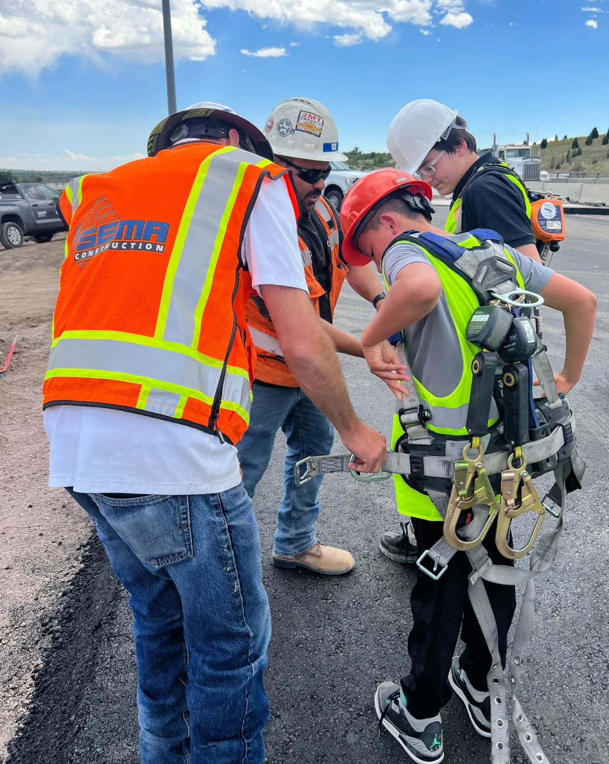 Two SEMA team members help two NIST students attach their harnesses correctly.