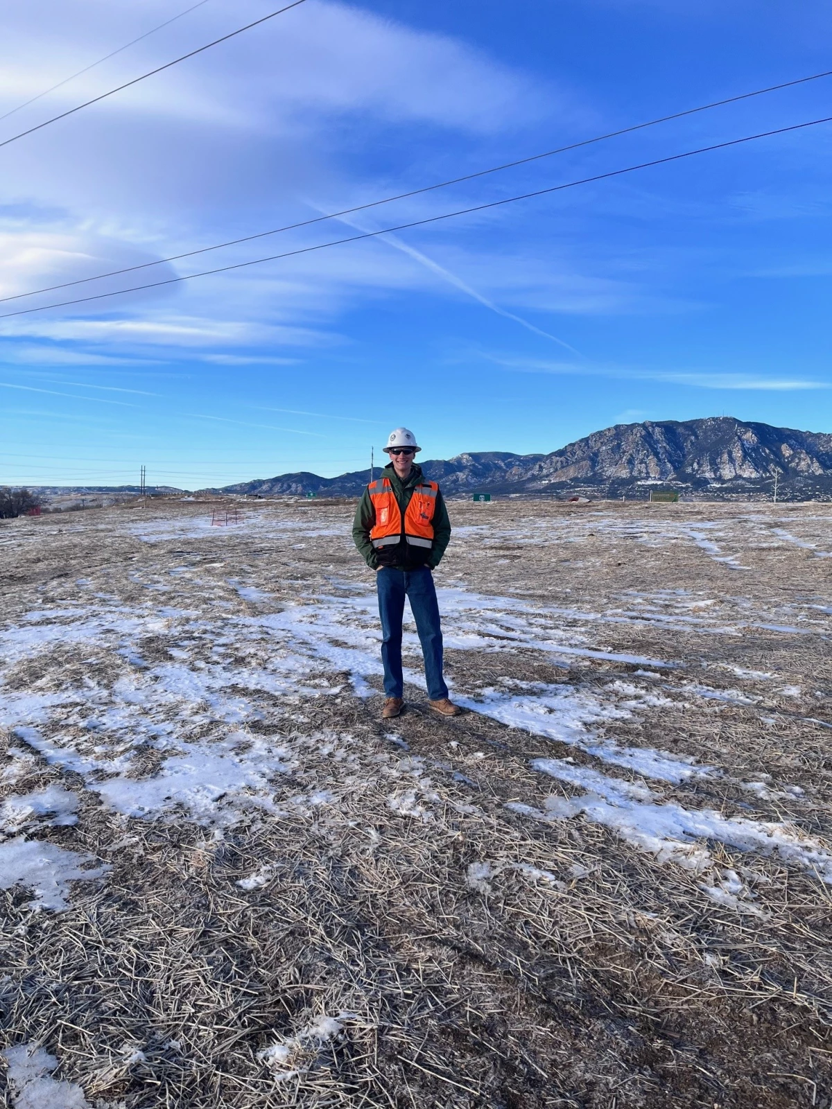Slade stands in a field in winter, wearing a high visibility jacket and hard helmet.